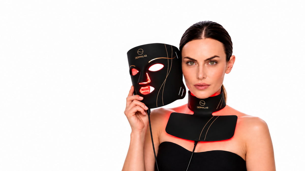 A woman holding a black LED light therapy face mask next to her neck and chest device, which also features a matching black neck collar. The devices have gold trim and red LED light accents, set against a solid white background.